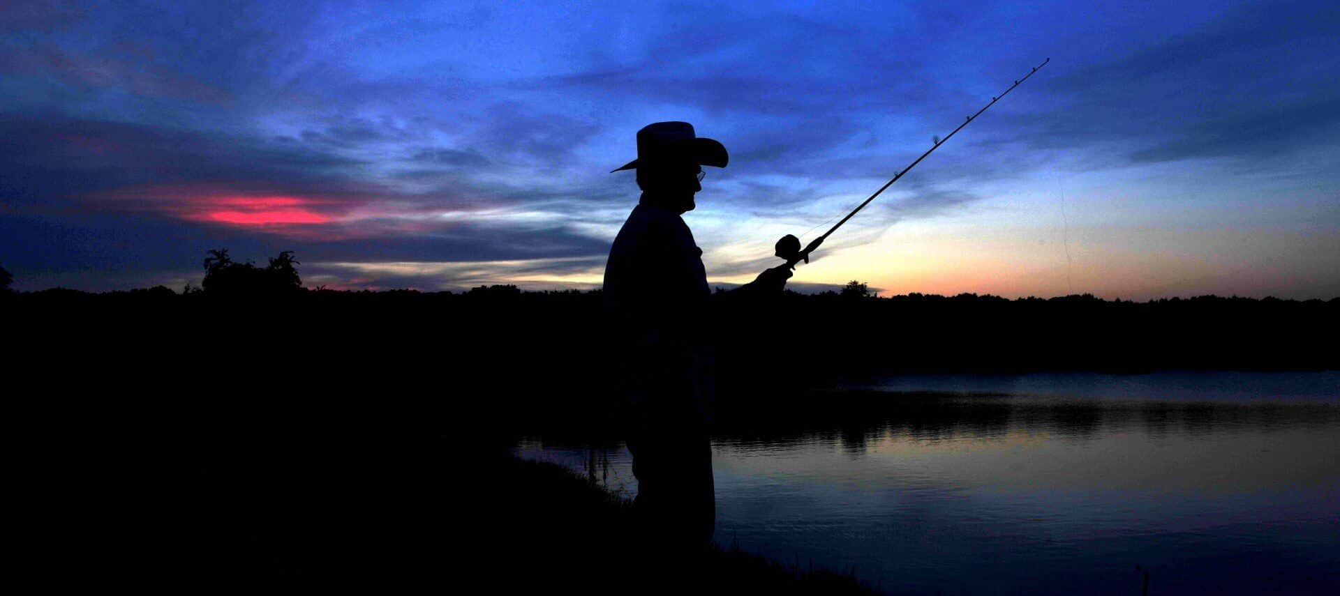 The silhouette of a man fishing on a pond at sunset