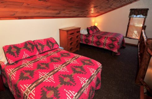 Upper loft bedroom area with twoo queen beds in matching red quilts with dressers and one window