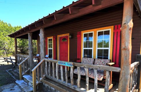 Brown cabin with red and yellow trim, front porch with wood railing and tree trunk posts