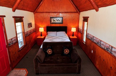 Cabin bedroom with a-frame roof, queen bed, sides tables with lamps and a brown loveseat