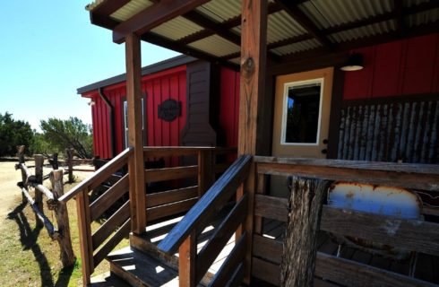 Front porch of a red cabin with wood railing and fencing