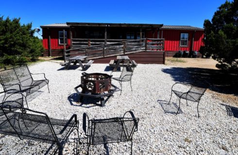 Backyard area behind a cabin with two picnic tables, fire pit and wrought iron seating