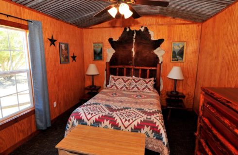 Cabin bedroom with tin roof, queen bed with quilt, side tables with lamps and large animal rug on wall