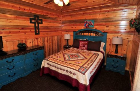 Cabin bedroom wit wood paneled walls, blue table and dresser and small TV