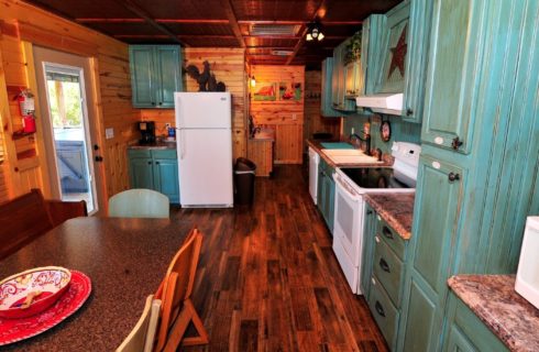 Cabin kitchen with wood floors and walls, table with bench and chairs and green cabinetry