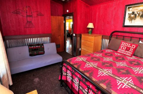 Cabin bedroom with red walls, queen bed, futon sofa and brown dresser
