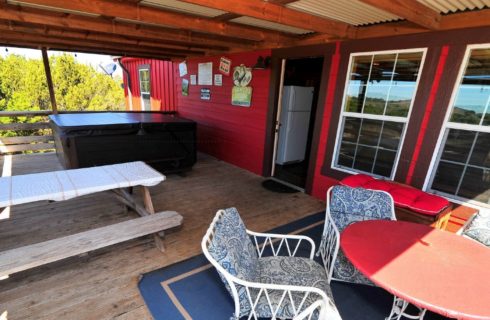 Outdoor patio of a cabin with table and chairs, picnic table and large hot tub