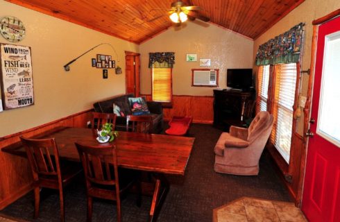 Living area of a cabin with table and chairs, couch, chair and TV on a dresser