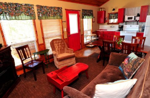 Kitchen area of a cabin with cherry cabinets, table and chairs and adjoining living room