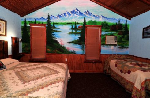 Cabin bedroom with queen bed, twin bed and large mountain mural on a wall with two windows