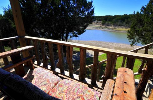 Front porch of a cabin with a loveseat overlooking a pond and trees