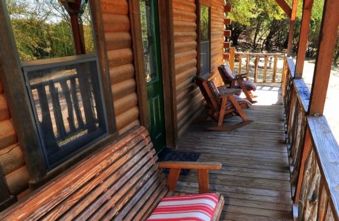 Front porch of a log cabin with rocking chairs and bench