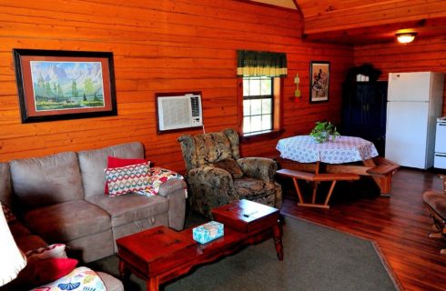 Interior of a cabin with kitchen, table with benches, couch and chair, coffee table and rocker
