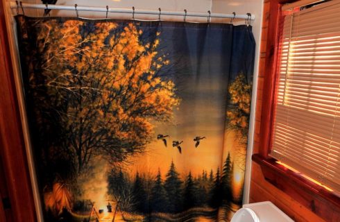 Bathroom with shower, nature themed curtain, shaded window over toilet