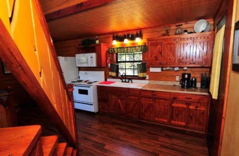 Cabin kitchen with gorgeous farmhouse style cabinetry, vanity lights over sink and stairway to an upper loft