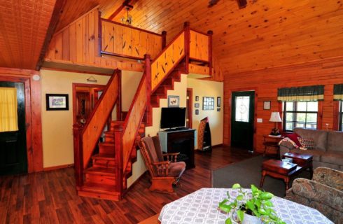 Interior of a large, open floor plan cabin with living room, kitchen table and stairway to an upper loft