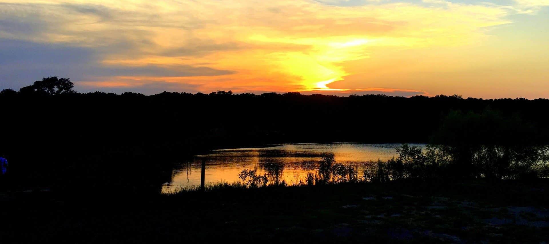 A small pond at sunset with bright orange and yellow skies