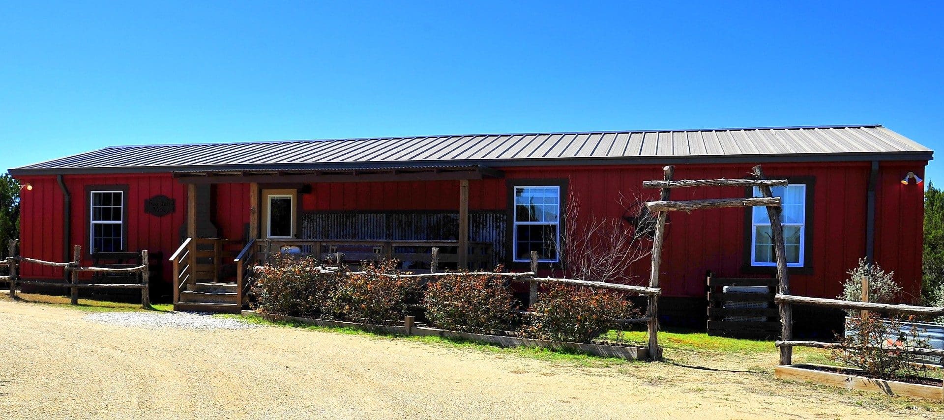 Long red cabin with wood fence ad bushes by a curved drive way