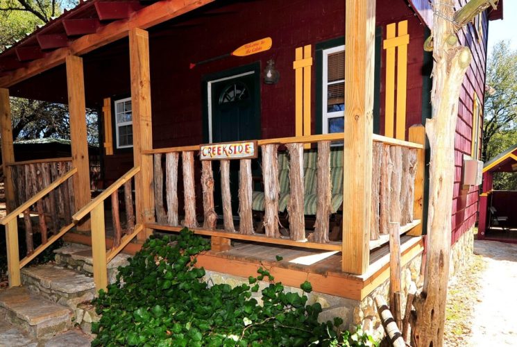 Small red cabin with yellow trim, front porch and red building behind at the end of a walkway