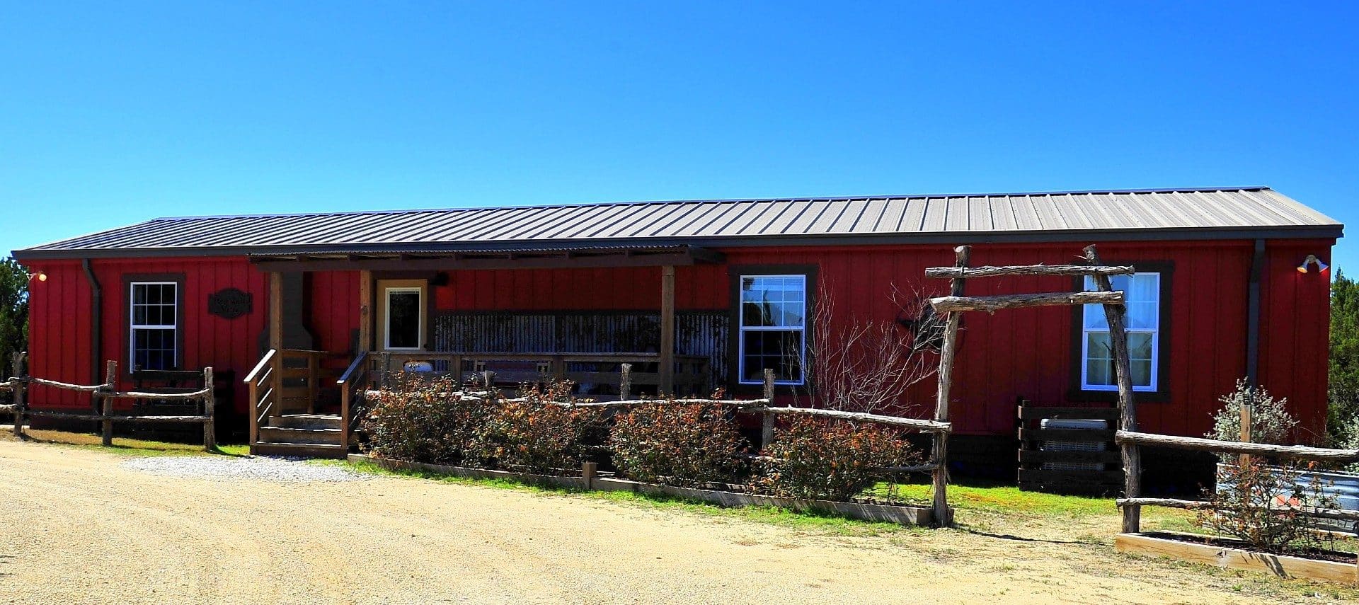 Long red cabin with wood fence ad bushes by a curved drive way