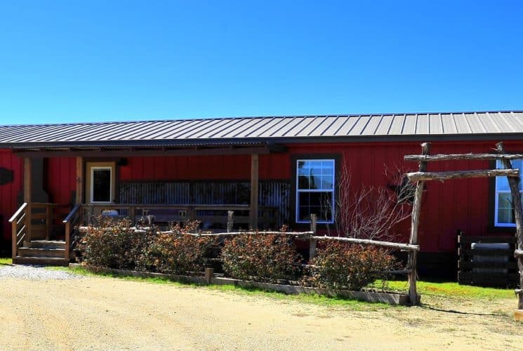 Long red cabin with wood fence ad bushes by a curved drive way