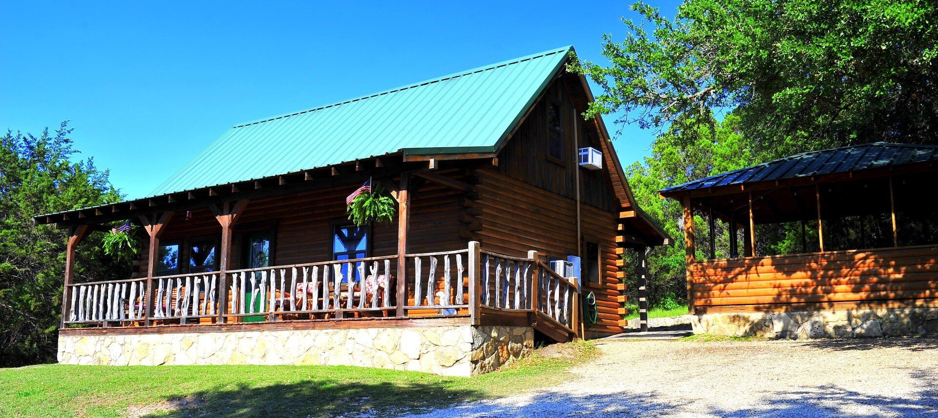 Wood log cabin with green roof, front porch with railing and side building with open air windows