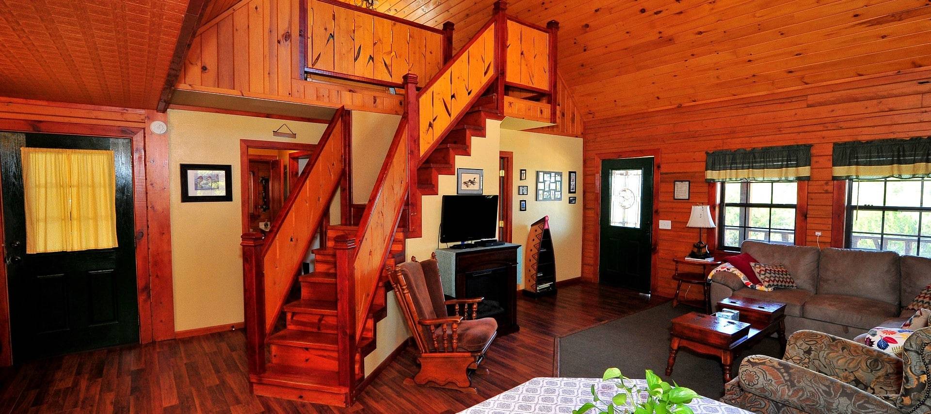 Interior of a large, open floor plan cabin with living room, kitchen table and stairway to an upper loft